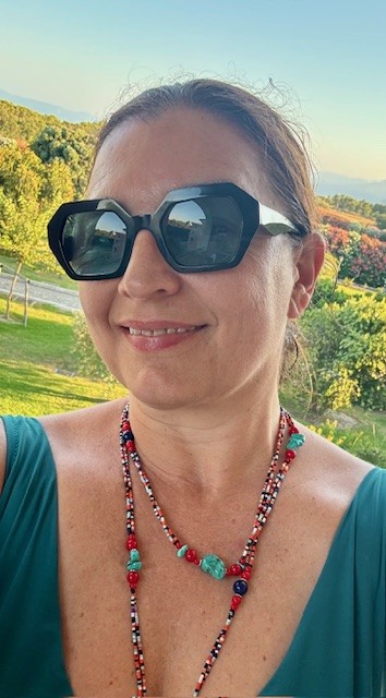 Aleksandra Pikula at golden hour in Sardinia &mdash; vineyard backdrop, warm light, smiling toward the camera.